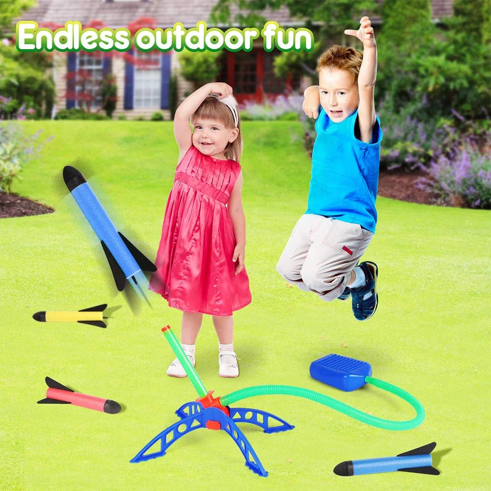 A boy and a girl are playing with an air-powered stomp rocket launcher and various related accessories in a green yard.