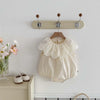 A cream-colored baby girl sleeveless jumpsuit with a lace collar hanging on a wall rack.