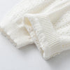 A close-up of a white knitted cotton cardigan featuring a ribbed cuff and small perforated details.