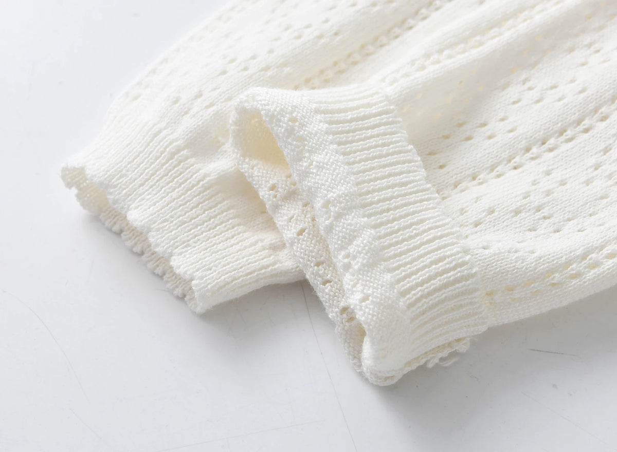 A close-up of a white knitted cotton cardigan featuring a ribbed cuff and small perforated details.