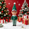 A festive elf decoration wearing a green hat and outfit stands in a snowy Christmas setting surrounded by wrapped gifts and a