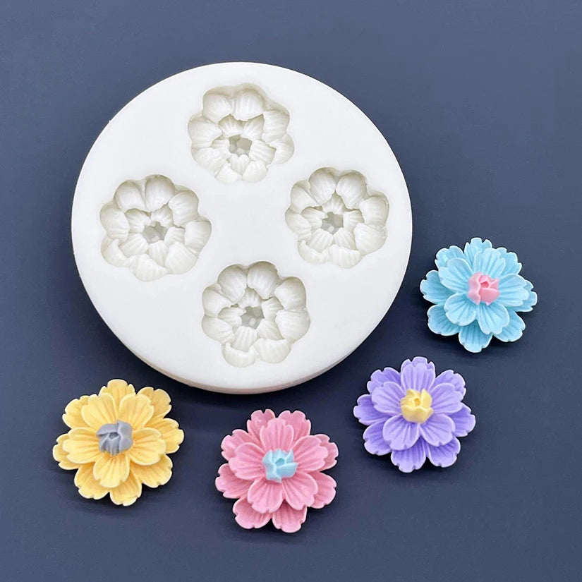 A white silicone mold with five embossed daisy flower shapes in varying shades of light green and blue, alongside colorful fo