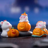 Three white and orange cartoon pumpkin bear figurines displayed on a dark surface against a blue background.
