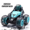 A black and teal remote control stunt car with large tires is shown on a cracked surface.