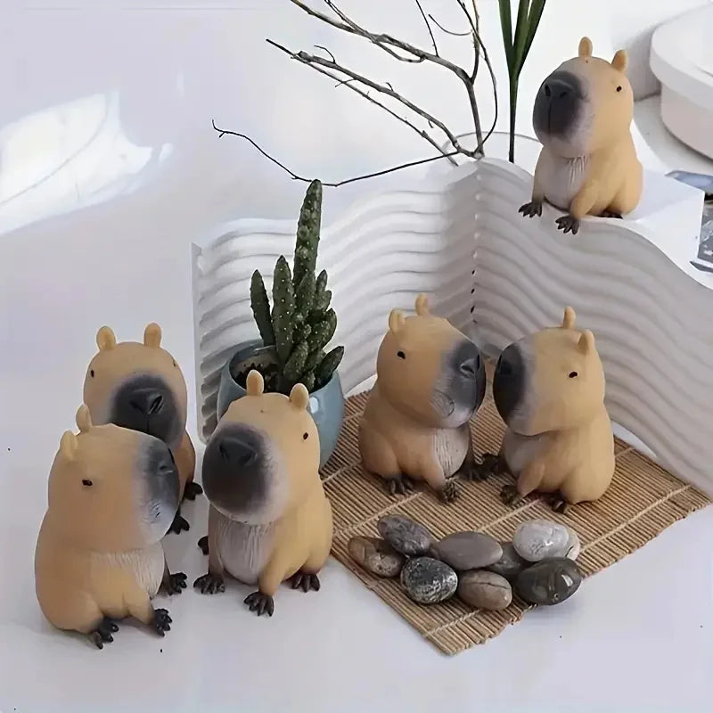 A collection of squishy capybara stress relief toys in various shades of tan and beige, displayed on a woven mat.