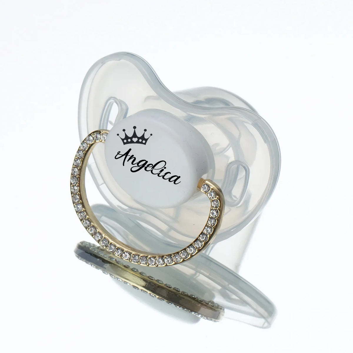 A clear silicone baby pacifier with a white center featuring the name Angelica and a gold rhinestone ring.
