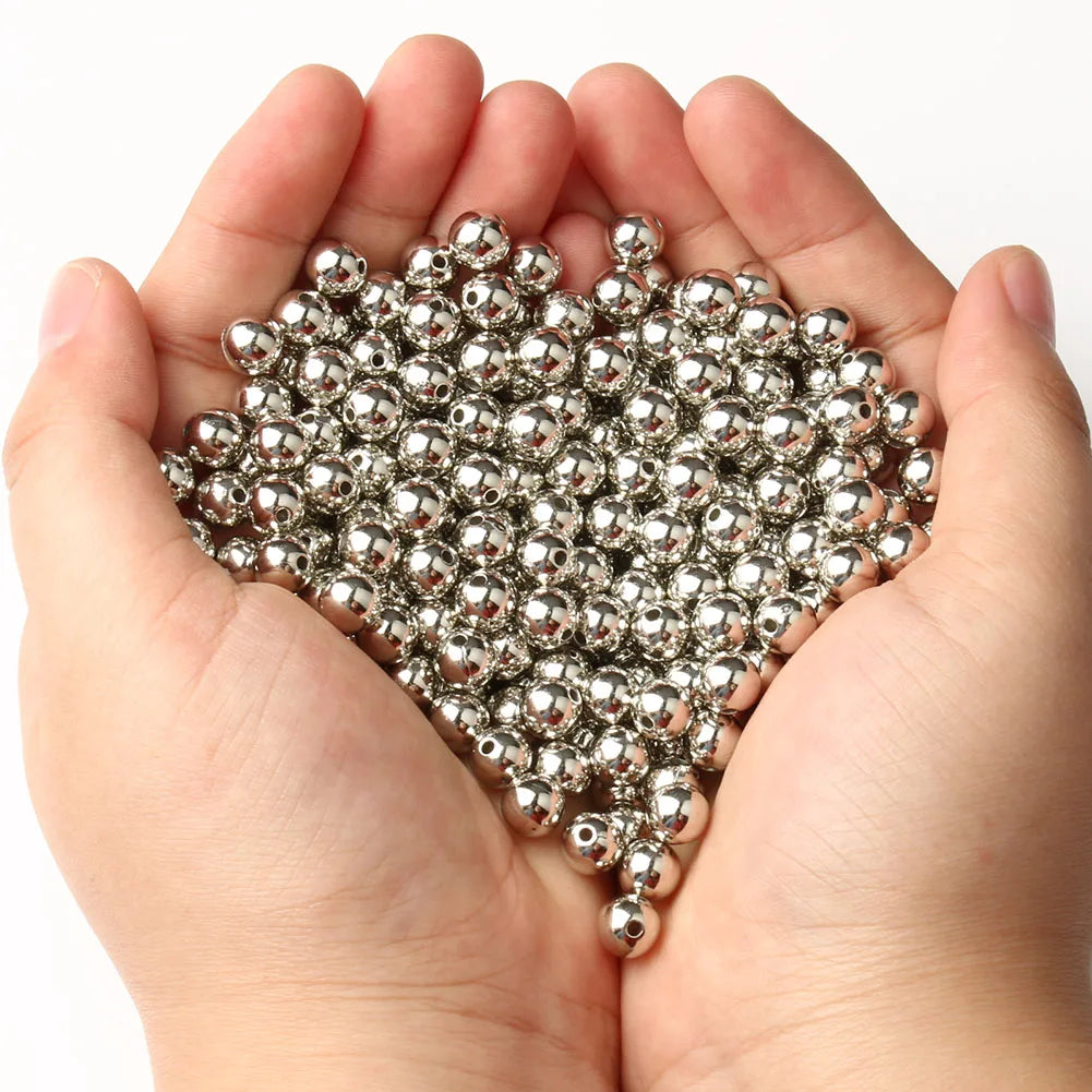 A pair of hands holds a pile of round silver spacer beads for DIY jewelry making