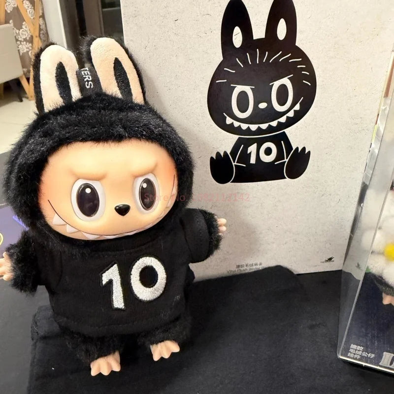A black plush toy resembling a rabbit with large eyes and white teeth, standing in front of a graphic featuring a black rabbi