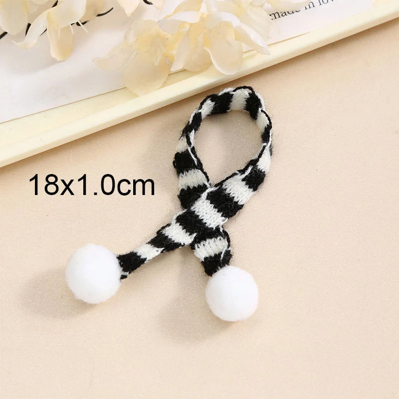 A black and white striped knit headband with white pom-poms, shown on a light background.