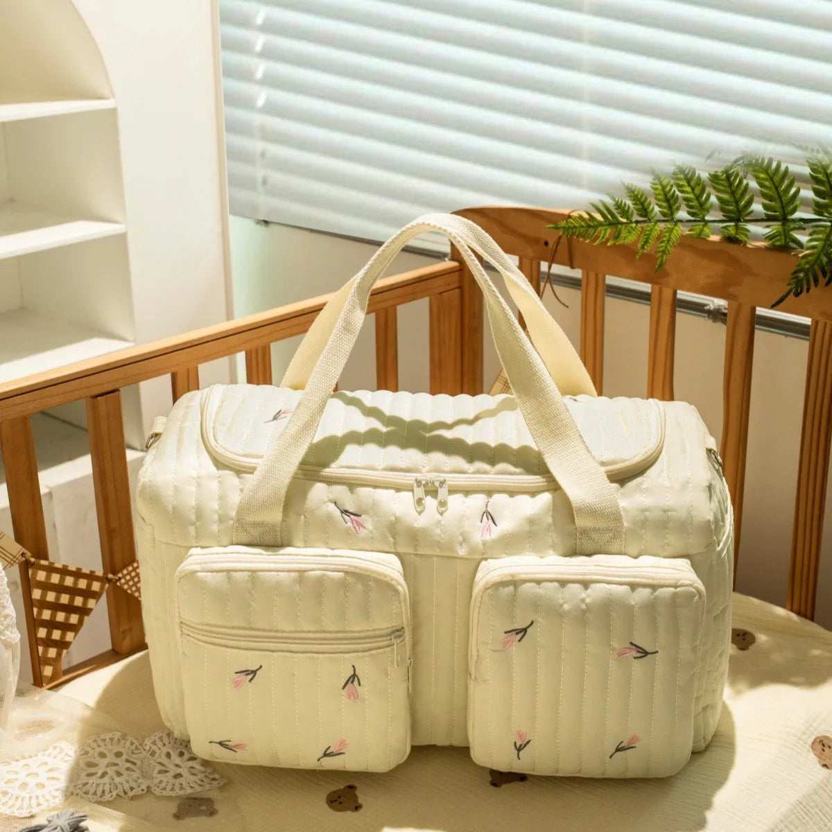 A cream-colored Enchanted Bear diaper bag resting on a light fabric next to wooden furniture.