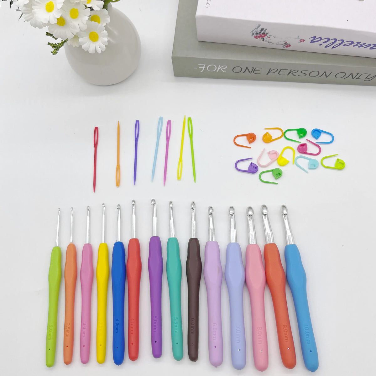 A collection of ergonomic crochet hooks, stitch markers, and needles in various colors laid out on a white surface.