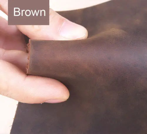 A hand is holding a piece of brown leather, showing the texture and color for crafting.