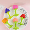A white plate holds several soft silicone fruit-shaped baby teethers in shades of pink, purple, and green.