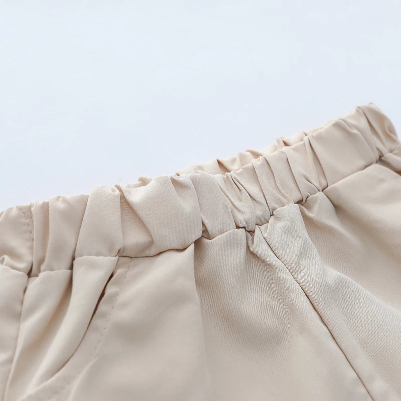 Close-up of a beige pleated fabric detail from a summer cartoon bear embroidered polo set for toddlers.