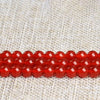 A string of natural red carnelian round beads for jewelry making placed on a light woven fabric background.