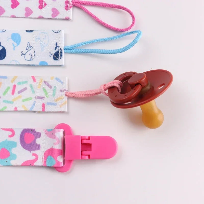 A set of four soft pacifier clips with double-sided prints in pink, blue, and white patterns.