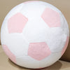 A white football plush pillow with pink accents, showing a close-up view of the ball's pattern.