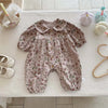 A floral doll collar baby girl long sleeve jumpsuit in pink and green patterns lying on a white surface.