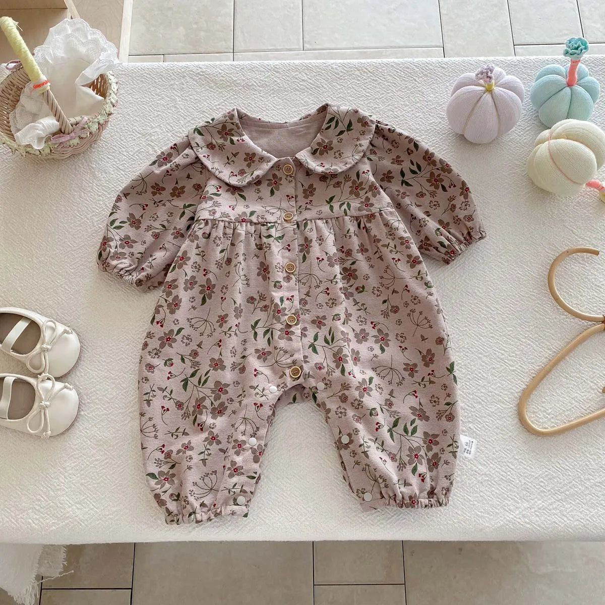A floral doll collar baby girl long sleeve jumpsuit in pink and green patterns lying on a white surface.