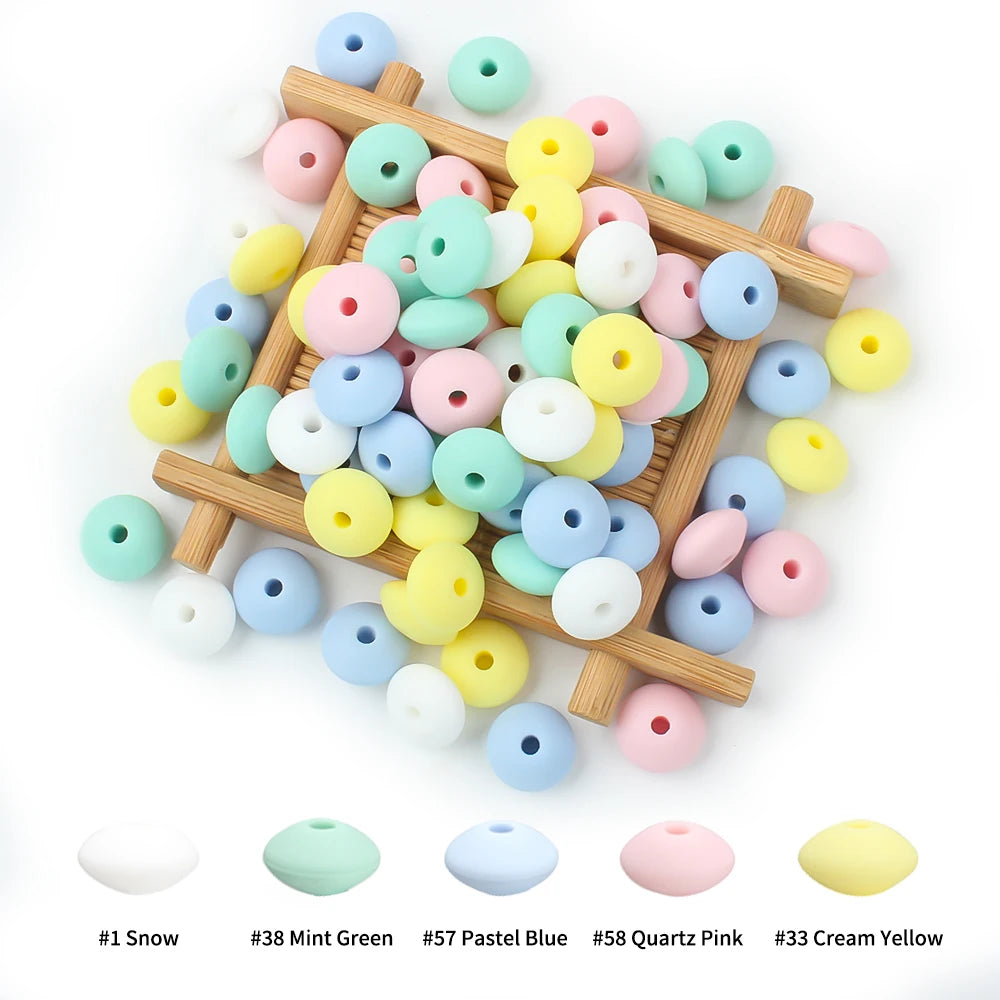 A collection of colorful silicone lentil beads in various shades including pink, blue, yellow, and white arranged on a wooden