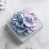 A cluster of light purple and blue flower petals arranged on a square white dish.