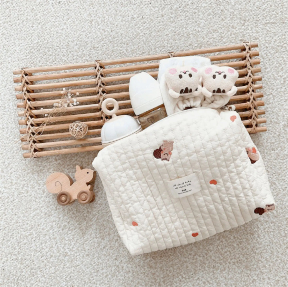 A quilted baby diaper caddy organizer with stroller straps and plush bear toys resting on a wooden slat tray.