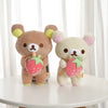 A pair of brown and cream Rilakkuma anime plush bears with pink strawberry accents sitting on a white surface.