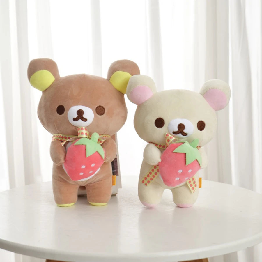 A pair of brown and cream Rilakkuma anime plush bears with pink strawberry accents sitting on a white surface.