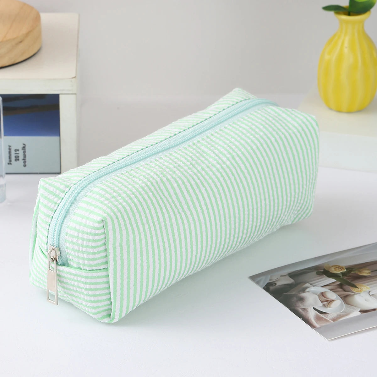 A light green and white striped canvas pencil case with a zipper is shown on a white surface.