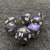 A collection of seven iridescent acrylic polyhedral dice scattered on a dark gray surface.