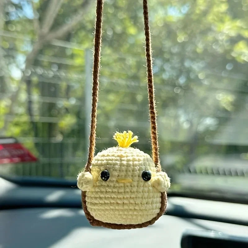 Handmade crochet yellow bird hanging ornament with brown string on a car window.