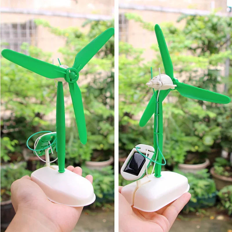A hand holds a green solar-powered DIY robot kit with spinning blades and electronic components in an outdoor garden setting.