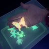 A hand holds a glow-in-the-dark butterfly and several glowing water elf figures on a translucent tray.