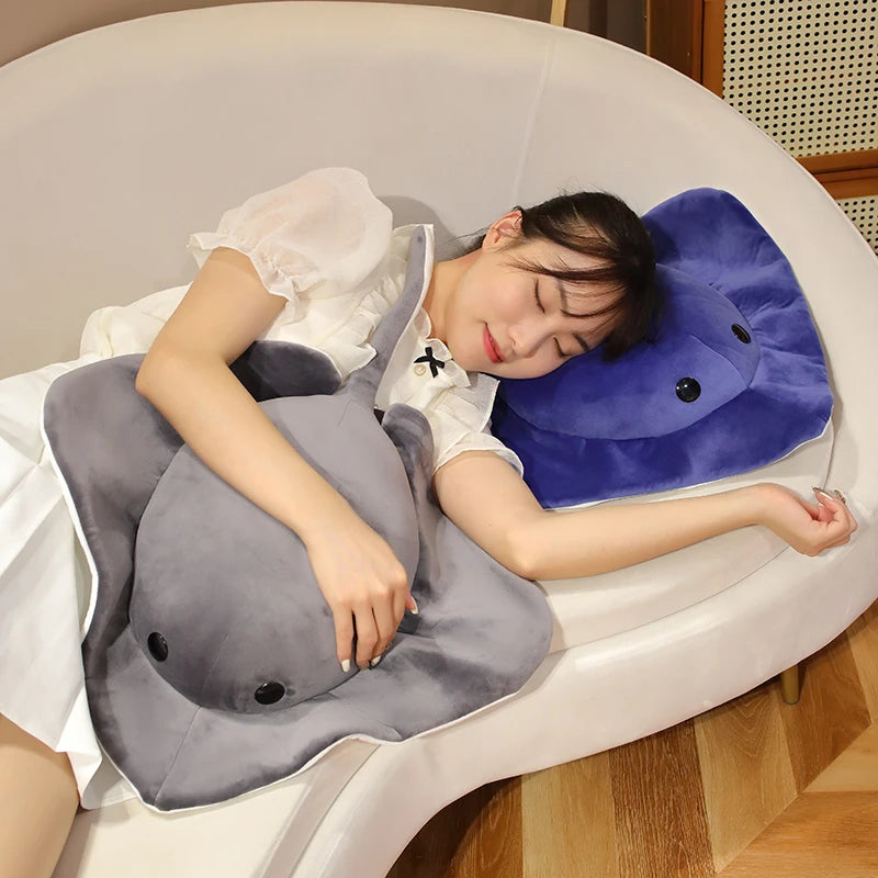 A person is relaxing in a white inflatable pool, holding a gray plush toy shaped like a devil fish.