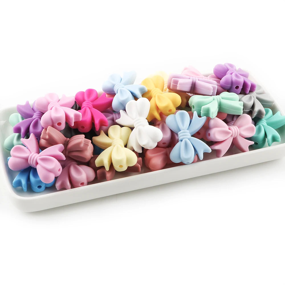 A collection of colorful silicone bow tie beads in various shades including pink, purple, yellow, and blue.