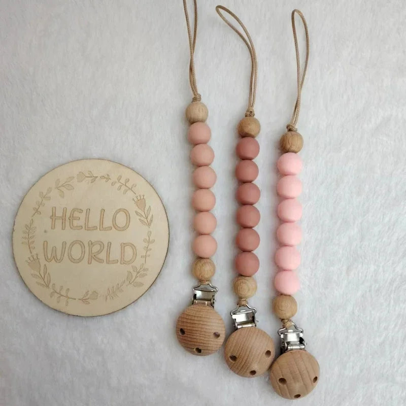 A set of wooden bead pacifier clips with silicone teethers in pink and natural wood tones.