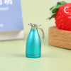 A miniature teal alloy kettle with a silver spout and handle, displayed next to a fresh strawberry.