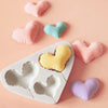 A set of silicone heart-shaped molds in pink, blue, and purple are displayed on a light pink surface.