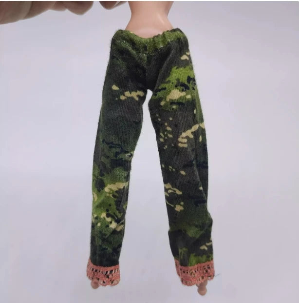 A doll wearing a green and camouflage patterned long-sleeved outfit.