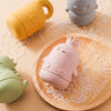 Pink silicone animal bath toy resting on a wooden tray surrounded by clear bath beads.