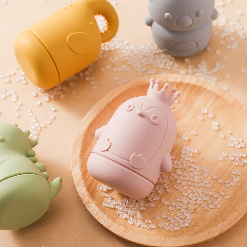 Pink silicone animal bath toy resting on a wooden tray surrounded by clear bath beads.