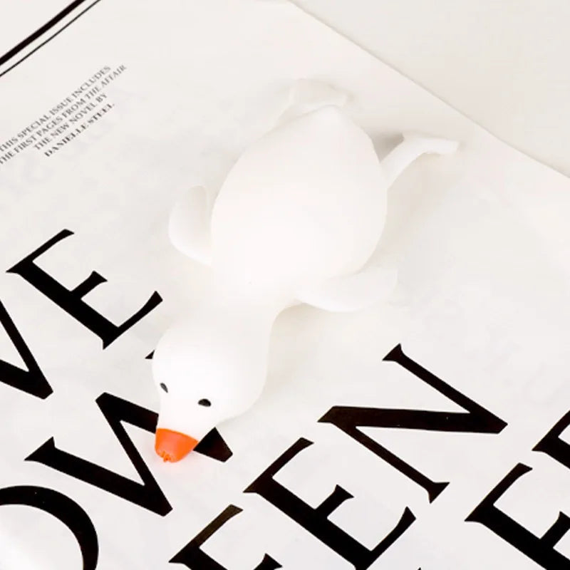 A white, soft duck squeeze toy is shown resting on a piece of paper with black text.