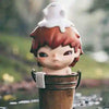 A small figure with reddish-brown hair and a white, fluffy head is shown emerging from a wooden container.