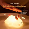 A soft white silicone rabbit night light illuminates a hand, demonstrating instant light activation for eye protection.