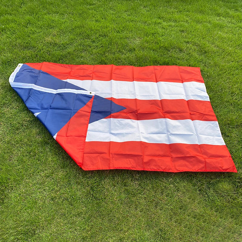 A red, white, and blue Puerto Rico national flag banner laid flat on green grass.