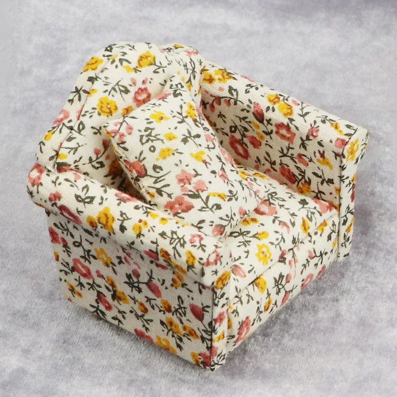 A miniature 1:12 scale sofa and pillow set for a dollhouse, featuring floral patterned fabric.