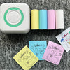 A white pocket thermal printer is shown next to several rolls of colored paper, including yellow, blue, and pink.