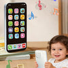 A baby is holding a white interactive learning phone toy with music notes floating around it.