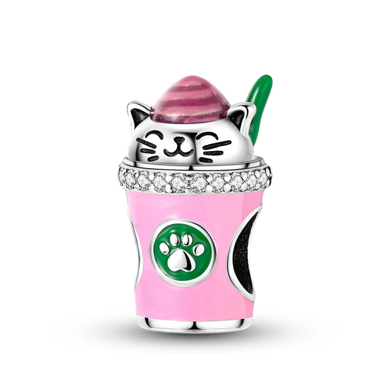 A silver cat-shaped charm bead with pink and green accents is displayed on a pink cup.