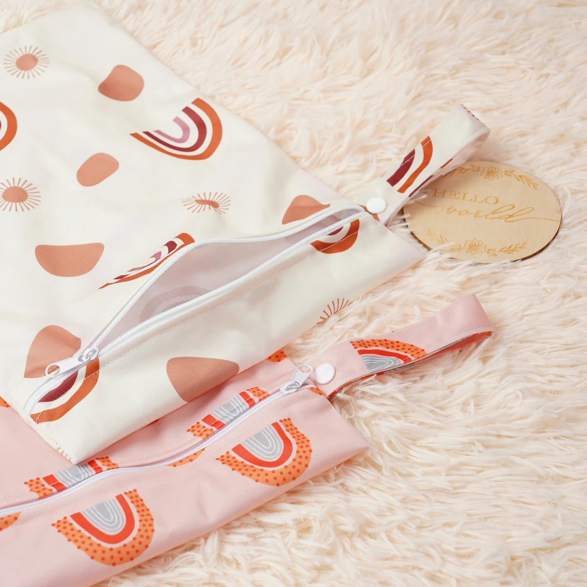 A set of two reusable waterproof baby wet bags featuring a light pink and white design with orange rainbow patterns.